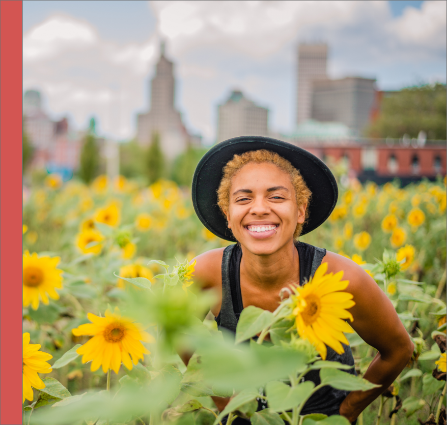 young woman in field of sunflowers with cityscape behind her