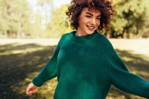 young woman in green sweater smiling as she walks through the park on a sunny day