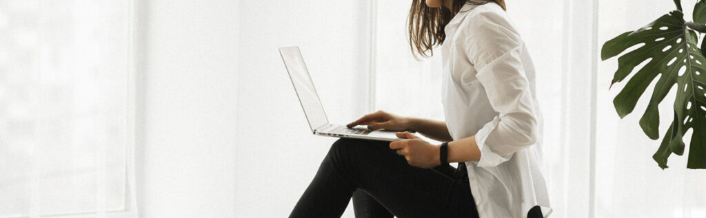 young woman sitting in clean, white walled office looking at a laptop