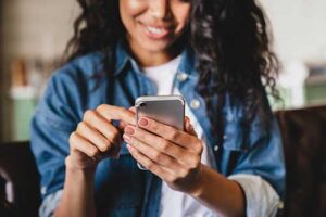 smiling young woman looking down at her smartphone as she searches for mental health services